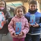Drei Kinder stehen glücklich mit Geschenken vor einem Auto