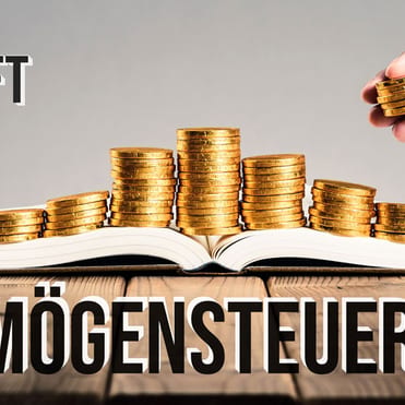 Ein geöffnetes Buch mit Münzen, die von einer Hand gestapelt werden, auf einem Holztisch mit der Aufschrift „Vermögensteuer" und „Verbindliche Auskunft vom 22. Nov. 2022".