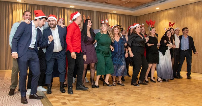 30 neue Mitarbeiter der PlattesGroup singen und tanzen auf der Weihnachtsfeier der Firma. Sie tragen alle festliche Kleidung und haben gute Laune